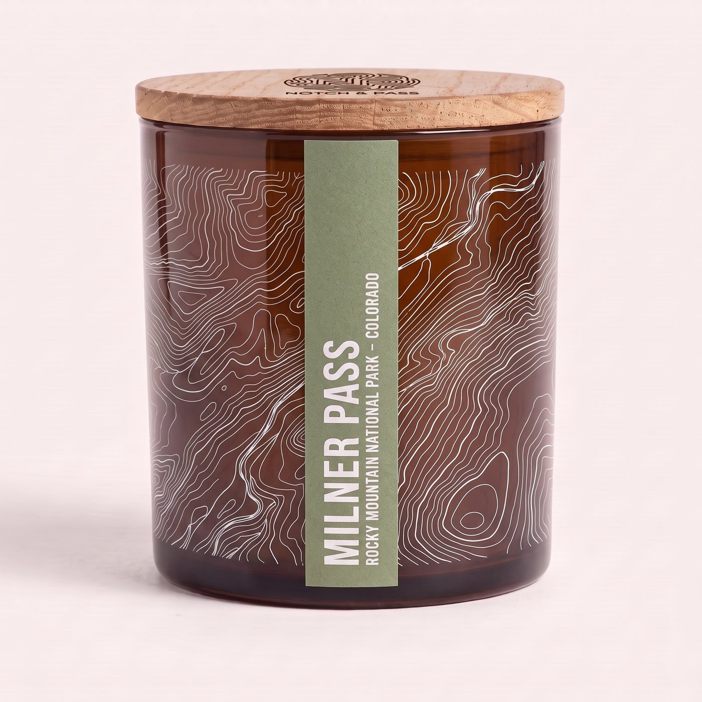 The Milner Pass candle: amber glass, its sheet printed in white, a sage estate-paper label, pine lid with the mark