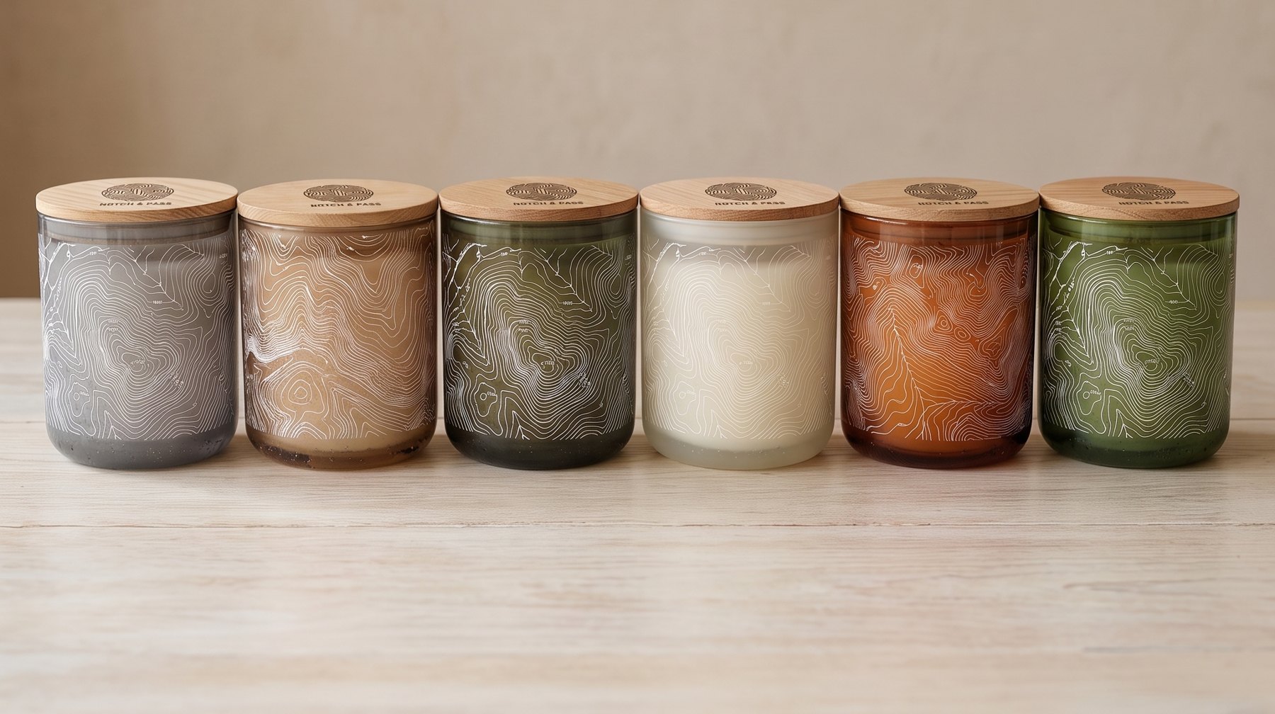 The six Trail candles in a row: the same rounded translucent glass in grey, sand, smoked olive, opaline cream, amber and moss green, white contours, pine lids