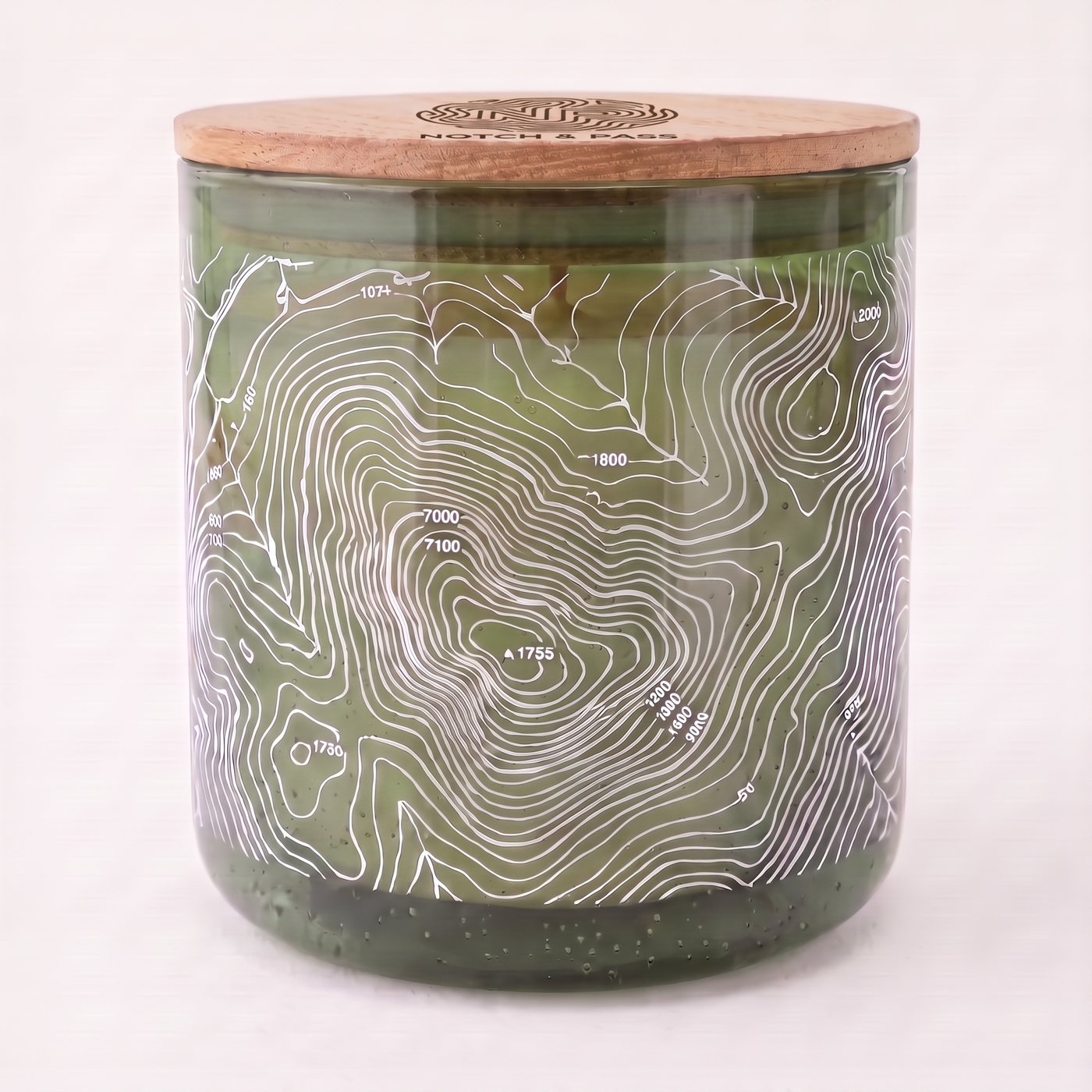 The Moss & Meltwater candle: moss-green glass, white contour print, pine lid with the mark burnt in